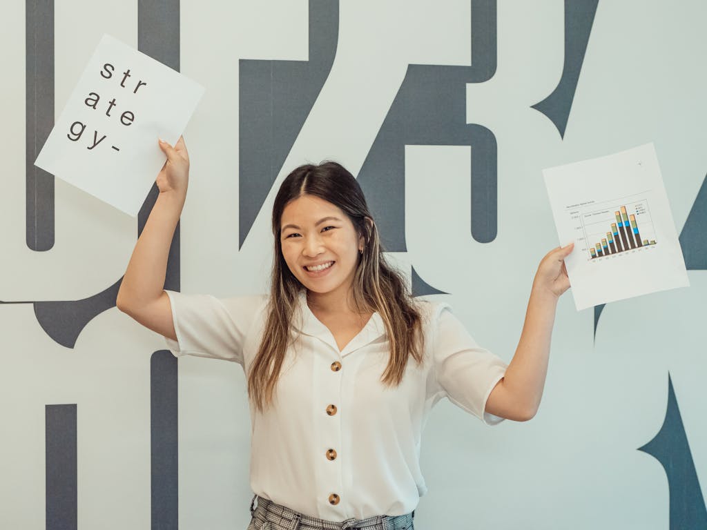 Smiling young woman in office holding business strategy documents, embodying enthusiasm and growth.